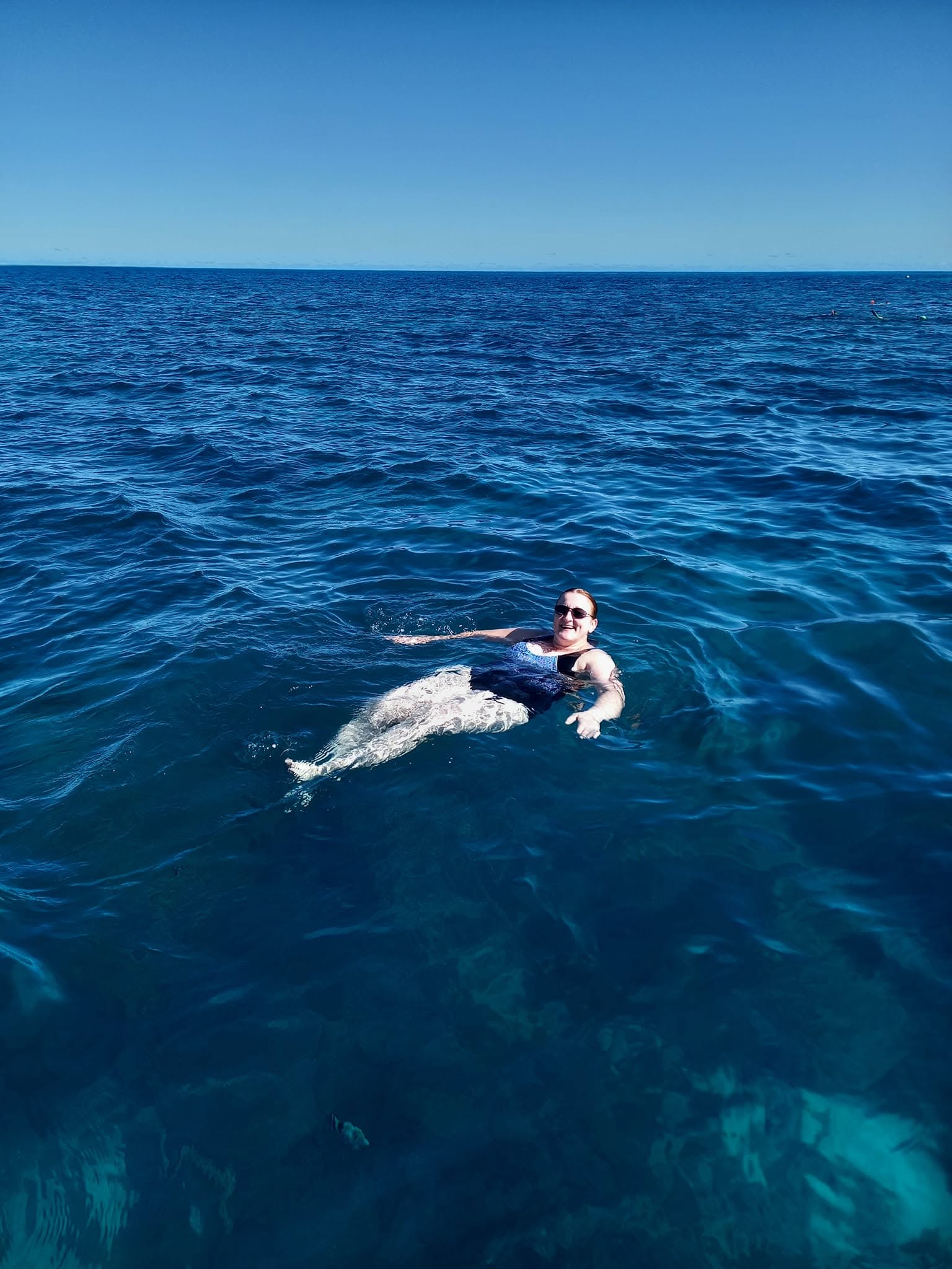 A smiling tourist floating on her back in the deep blue ocean waters of the Tantabiddi Sanctuary Zone at Ningaloo Reef.